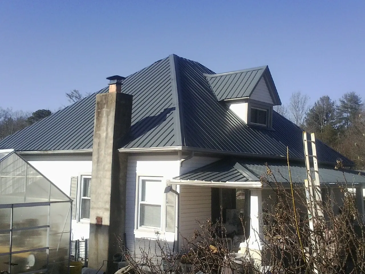 Dark blue standing seam metal roof on a white farmhouse with dormer — Slate & Tile Roof Repair by Roofing Brothers in Aurora