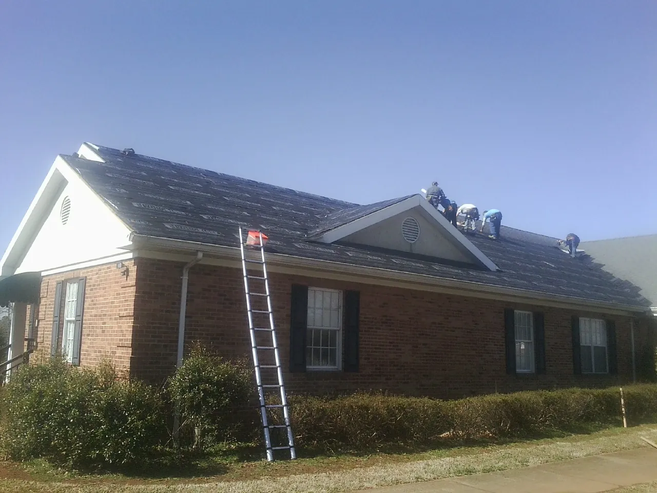 Crew tearing shingles off a brick ranch roof with a ladder set — Emergency Roof Repair work by our crew in Aurora